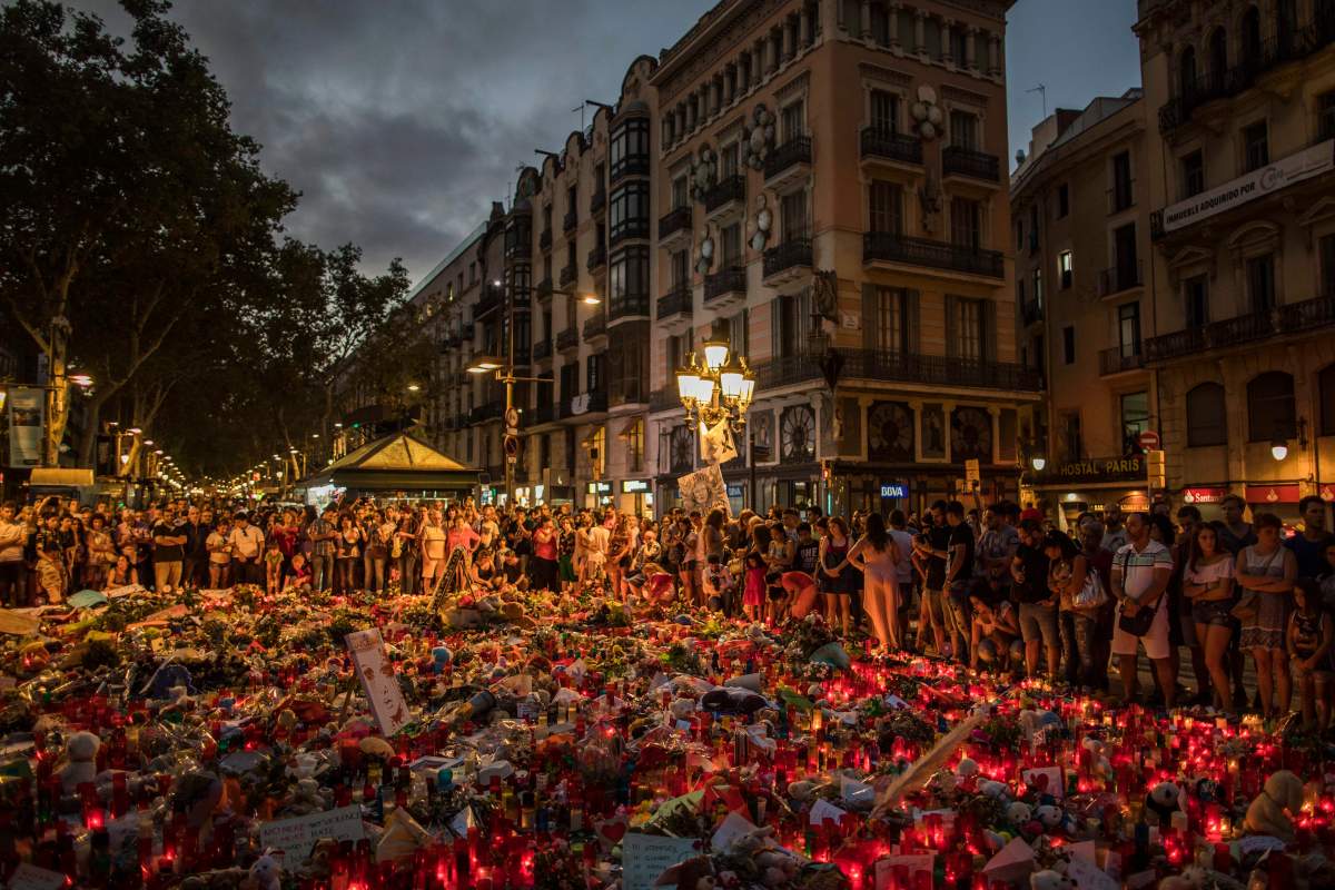People stand next to candles and flowers placed on the ground, after a terror attack that left many killed and wounded in Barcelona, Spain, Monday, Aug. 21, 2017. 