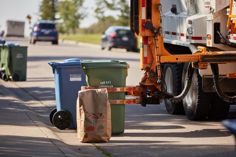 A City of Calgary truck collects a green cart composting bin.