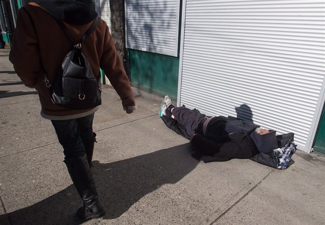 A woman walks past a man sleeping on the street in the Downtown Eastside of Vancouver, February 2017.