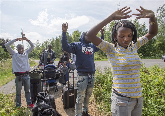 A group of asylum seekers raise their hands as they approach RCMP officers while crossing the Canadian border from Champlain, N.Y., Friday, August 4, 2017.