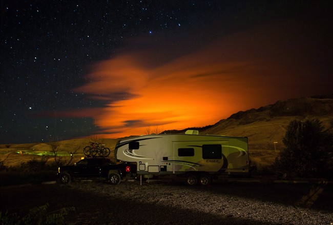 A trailer parked at a campground in Savona, B.C., is seen as the Elephant Hill wildfire burns in the distance near Clinton, illuminating smoke in the sky during the early morning hours of Sunday July 30, 2017. 