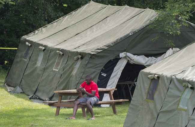 An asylum seeker checks his phone next to a tent at the Canada-United States border in Lacolle, Que. Thursday, August 10, 2017.