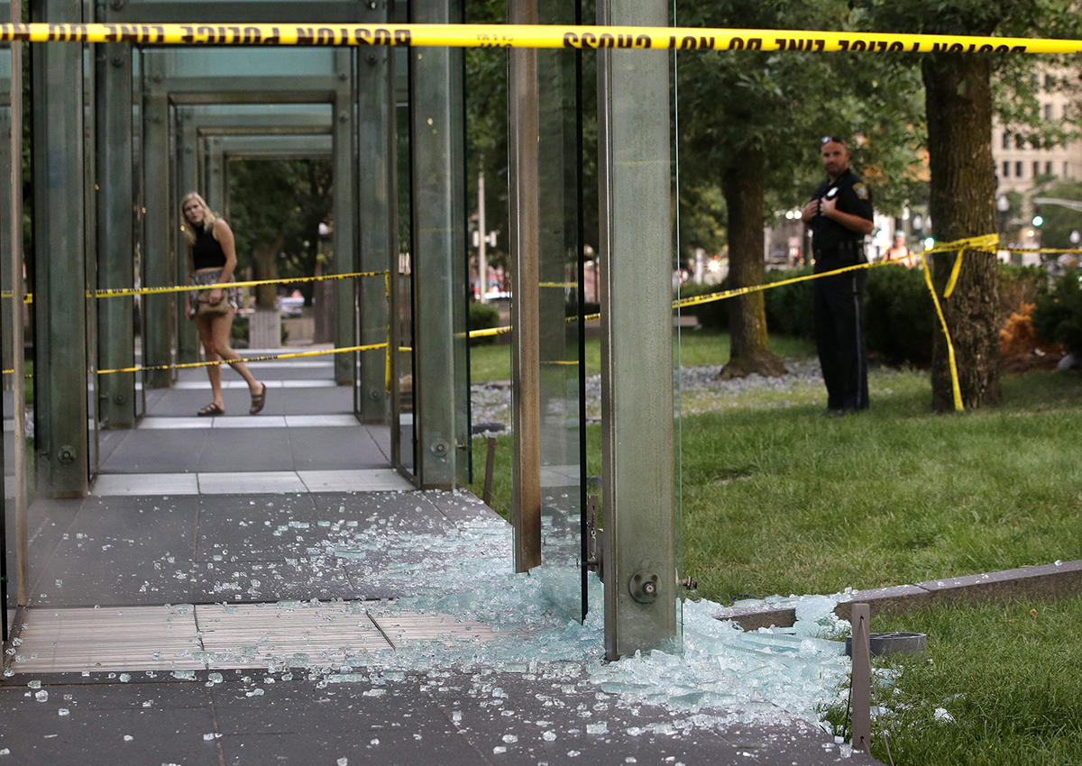 A passerby, left, and a law enforcement official, right, stand near broken glass at the New England Holocaust Memorial on Monday, Aug. 14, 2017, in Boston. 