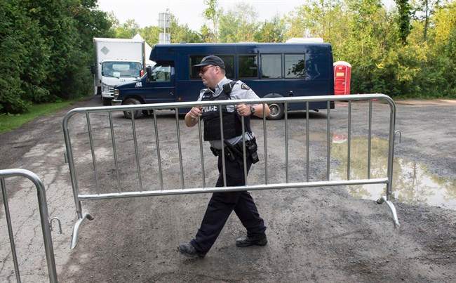 An RCMP officer moves a barricade as they wait for the arrival of asylum seekers crossing the border into Canada from the United States at a police checkpoint close to the Canada-U.S. border near Hemmingford, Que., on Thursday, August 3, 2017.