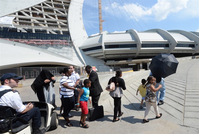 Asylum seekers take a walk outside Olympic Stadium as security guards look on in Montreal, Wednesday, Aug.2, 2017. The stadium will be housing asylum seekers after a spike in the number of people crossing at the United States border in recent months.