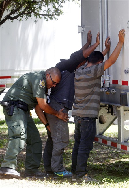 In this Sunday, Aug. 13, 2017, photo, a Border Patrol officer pats down several of the men that were found with a group of immigrants in a tractor-trailer in Edinburg, Texas. 