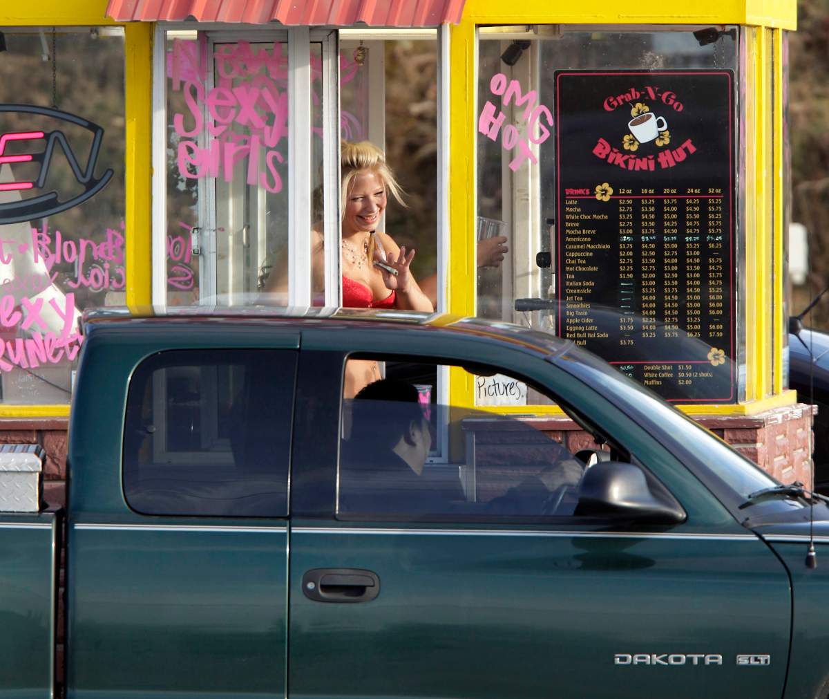 A barista at a Grab-N-Go Bikini Hut espresso stand holds money as she waves to a customer, just outside the city limits of Everett, Wash., in Snohomish County. 