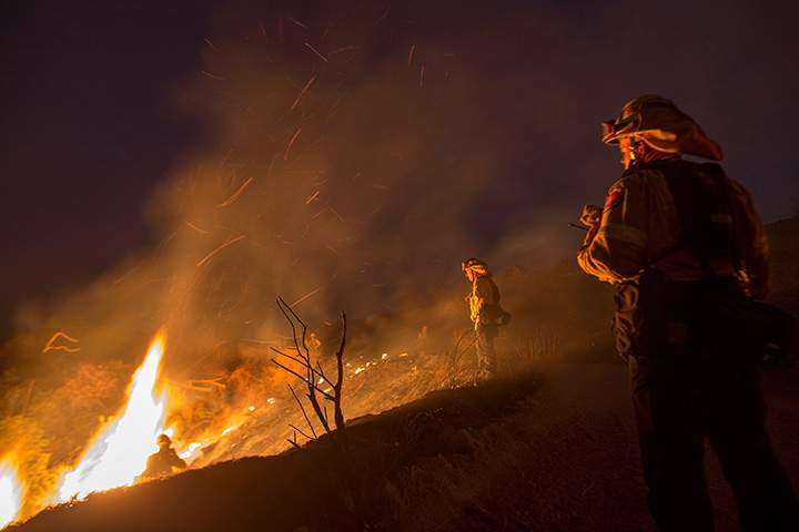 Firefighters watch a colleague emerge from fighting flames in chaparral brush at the La Tuna Fire on September 2, 2017 near Burbank, California.