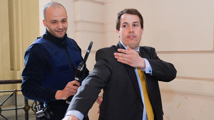 Laurent Louis, right, performs the controversial 'quenelle' gesture while going through security check at the Brussels' Justice Palace during a hearing at the Brussels' council chamber in Brussels.