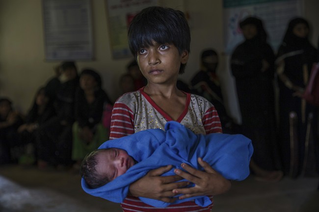 Rohingya Muslim girl Afeefa Bebi, who recently crossed over from Myanmar into Bangladesh, holds her few-hours-old brother as doctors check her mother Yasmeen Ara at a community hospital in Kutupalong refugee camp, Bangladesh, Wednesday, Sept. 13, 2017. The family crossed into Bangladesh on Sept. 3.