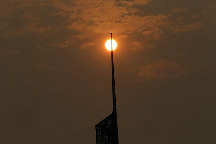 A glowing, orange sun, muted by wildfire smoke, is visible behind the spire of the Oregon Convention Center in Portland, Ore., Tuesday, Sept. 5, 2017.