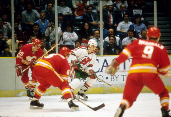 EAST RUTHERFORD, NJ - 1988:  George McPhee #21 of the New Jersey Devils skates with the puck as Lanny McDonald #9, Joe Nieuwendyk #25 and Ric Nattress #6 of the Calgary Flames defend during an NHL game circa 1988 at the Brendan Byrne Arena in East Rutherford, New Jersey.  (Photo by B Bennett/Getty Images).