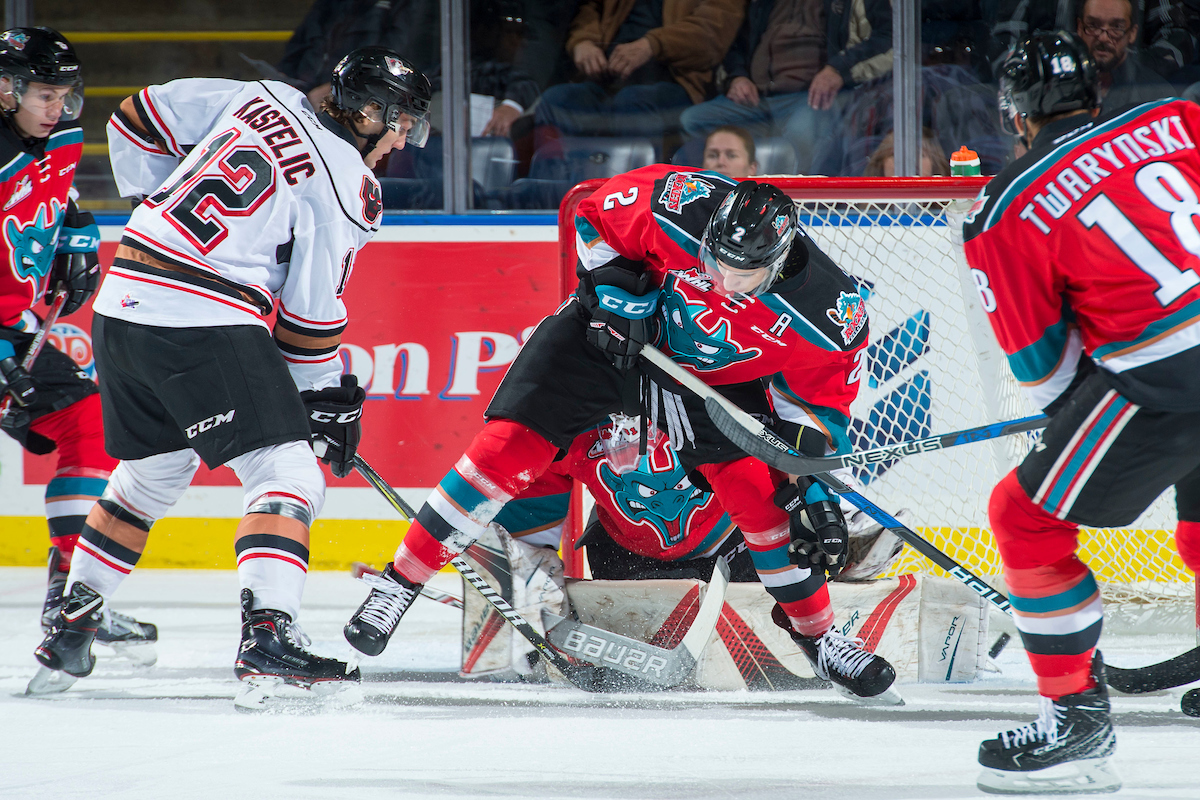 KELOWNA, CANADA - OCTOBER 13: Mark Kastelic #12 of the Calgary Hitmen puts the puck past James Hilsendager #2 and Brodan Salmond #31 of the Kelowna Rockets and scores a first period goal on October 13, 2017 at Prospera Place in Kelowna, British Columbia, Canada.  (Photo by Marissa Baecker/Shoot the Breeze)  *** Local Caption ***.