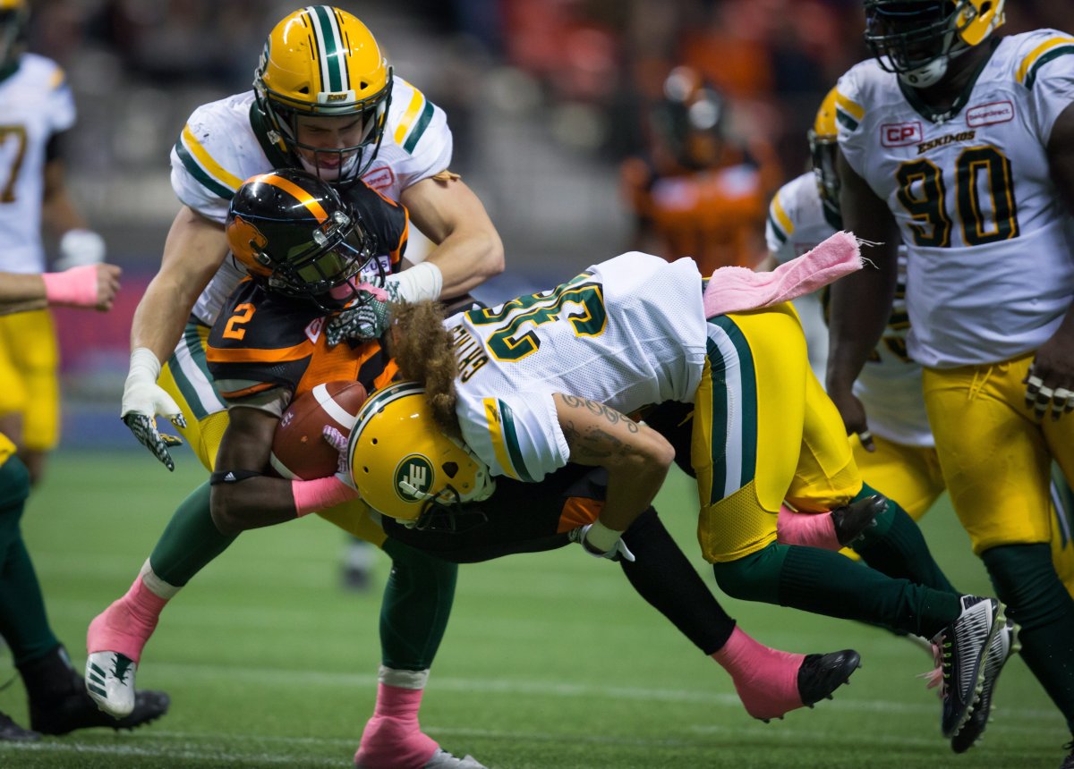 Edmonton Eskimos' Adam Konar, back left, and Aaron Grymes, right, tackle B.C. Lions' Chris Rainey (2) during the second half of a CFL football game in Vancouver, B.C., on Saturday October 21, 2017.