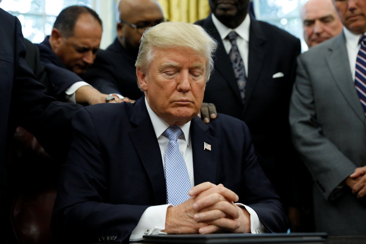 Faith leaders place their hands on the shoulders of U.S. President Donald Trump as he takes part in a prayer for those affected by Hurricane Harvey in the Oval Office of the White House in Washington, U.S., September 1, 2017.