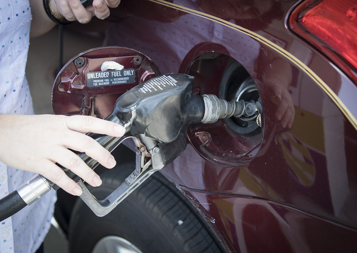 Woman's hand holding a pump nozzle in car fuel tank door.