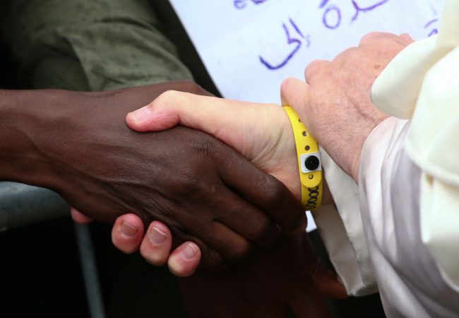 Pope Francis wears a yellow plastic ID bracelet as he shakes hands during a visit to a migrant reception centre in Bologna, Italy, Oct. 1, 2017.