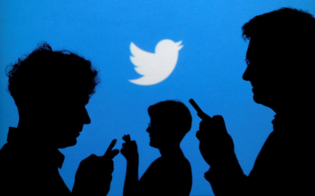 People holding mobile phones are silhouetted against a backdrop projected with the Twitter logo in this illustration picture.