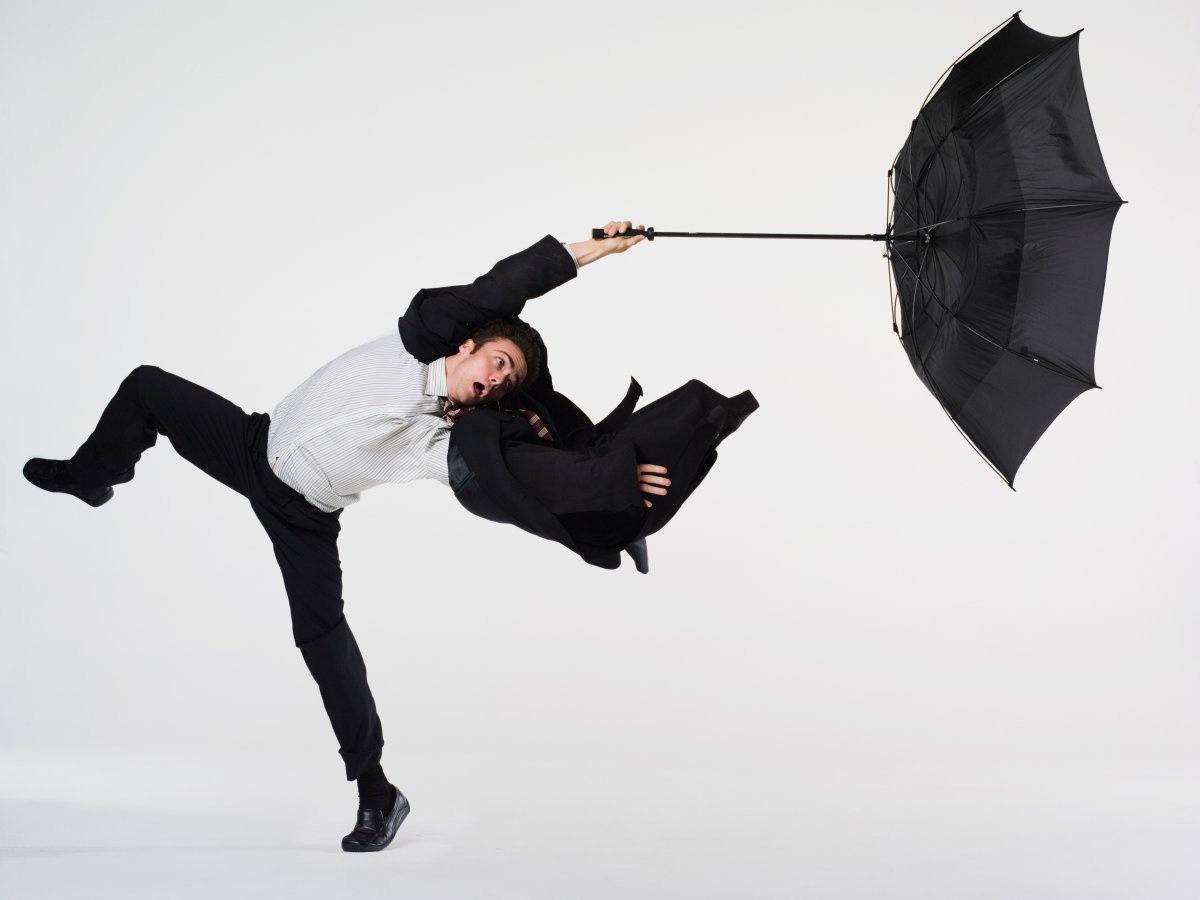 Young businessman caught in high winds, umbrella being blown out.