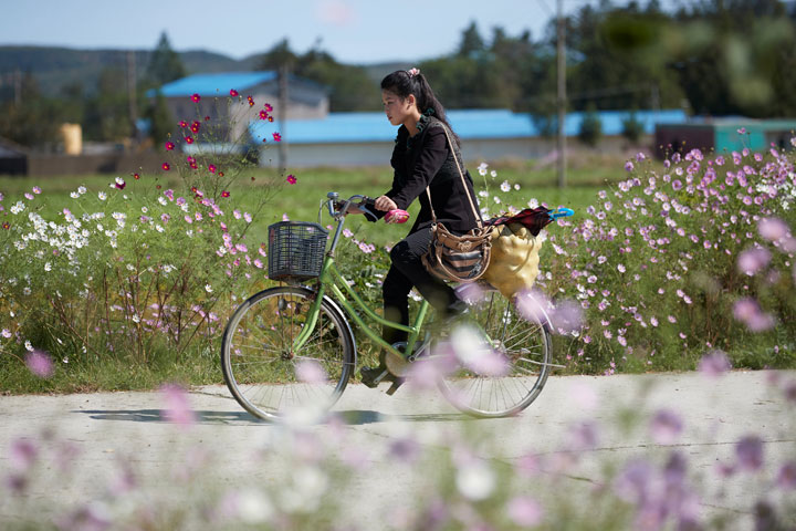 A girl carrying goods cycles past wild flowers