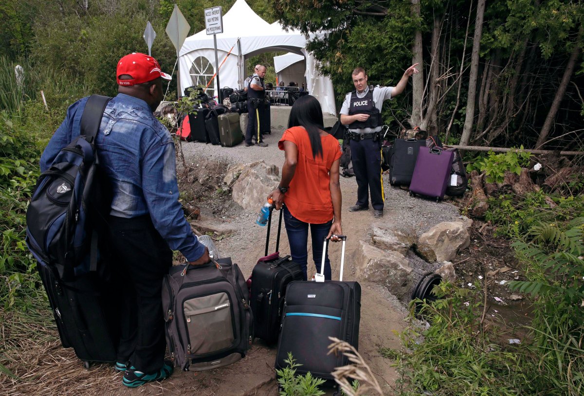 In this Aug. 7, 2017 file photo, a Royal Canadian Mounted Police officer informs a migrant couple of the location of a legal border station, shortly before they illegally crossed from Champlain, N.Y., to Saint-Bernard-de-Lacolle, Quebec, using Roxham Road. Authorities say more than 80 percent of the 4,000 migrants who crossed into Quebec recently are from Haiti, and the rest include people from India, Mexico, Colombia and Turkey. (AP Photo/Charles Krupa, File).