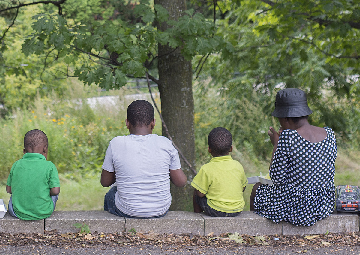 Women and children eat food handed out by a local Haitian church in a park next to the Olympic Stadium in Montreal on Thursday, August 31, 2017. 