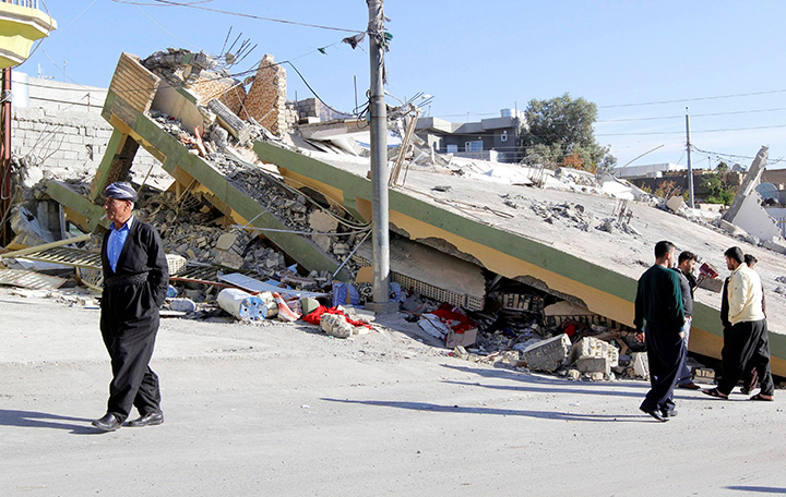 People walk past a damaged building following an earthquake in the town of Darbandikhan, Iraq November 13, 2017.