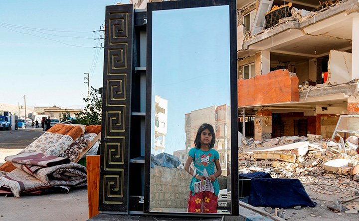 A young girl looks through a salvaged mirror from a damaged building in the town of Sarpol-e Zahab on November 14, 2017, following a 7.3-magnitude earthquake.