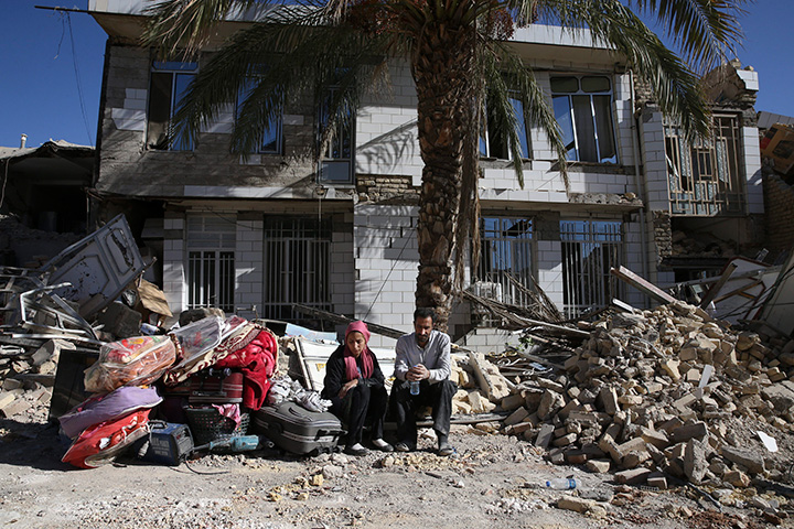 Survivors sit in front of a destroyed house following an earthquake in Sarpol-e-Zahab in western Iran, Tuesday, Nov. 14, 2017.