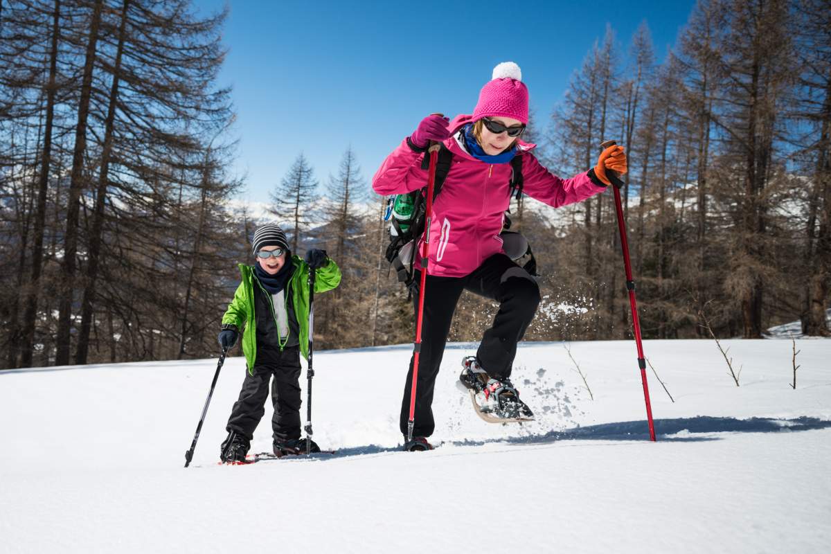 Young woman and her little son snowshoeing in a sunny day.