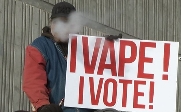 A protester vapes while holding a protest sign.