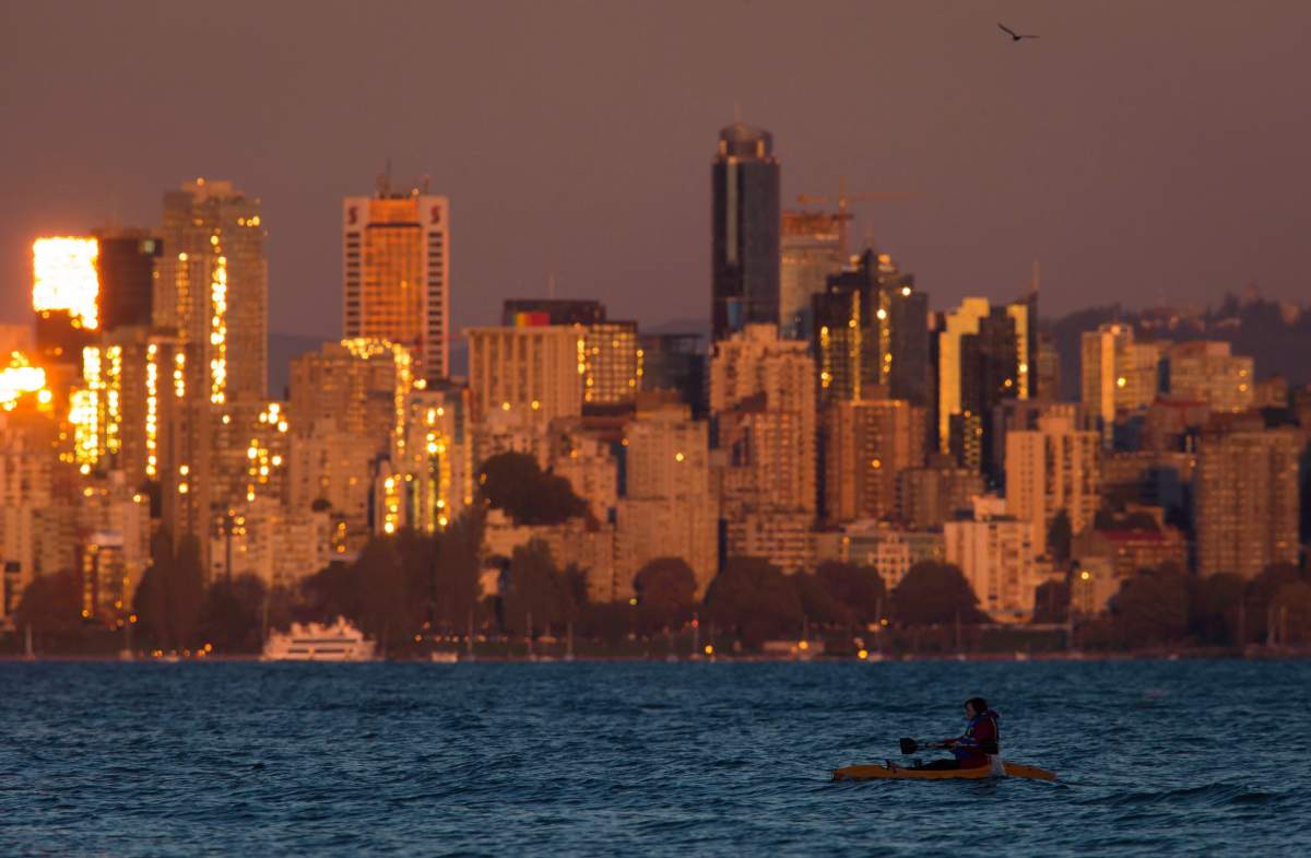 A woman paddles a kayak on the waters of English Bay as the sun reflects off windows on buildings in downtown Vancouver, B.C., at sunset on Sunday, September 27, 2015. 