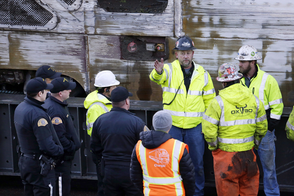 Police officers and workers gather before transporting the engine from an Amtrak train crash two days earlier away from the scene, Dec. 20, 2017, in DuPont, Wash.   