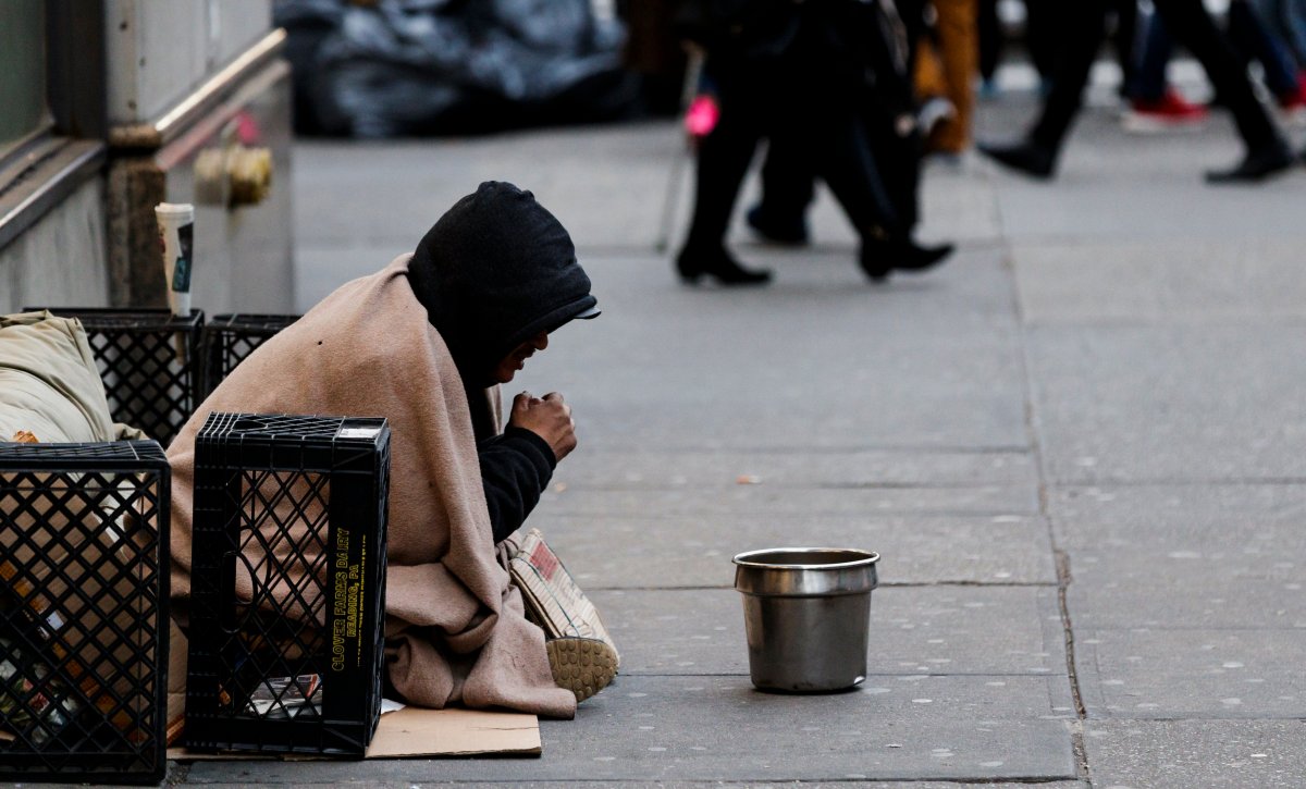 A man sits on a sidewalk hoping for spare change in New York City.