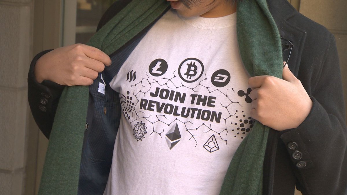 A man wears a T-shirt showing off several cryptocurrency logos.