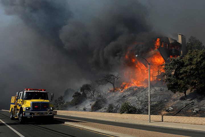 A fire crew passes a burning home during a wind-driven wildfire in Ventura, California, December 5, 2017.