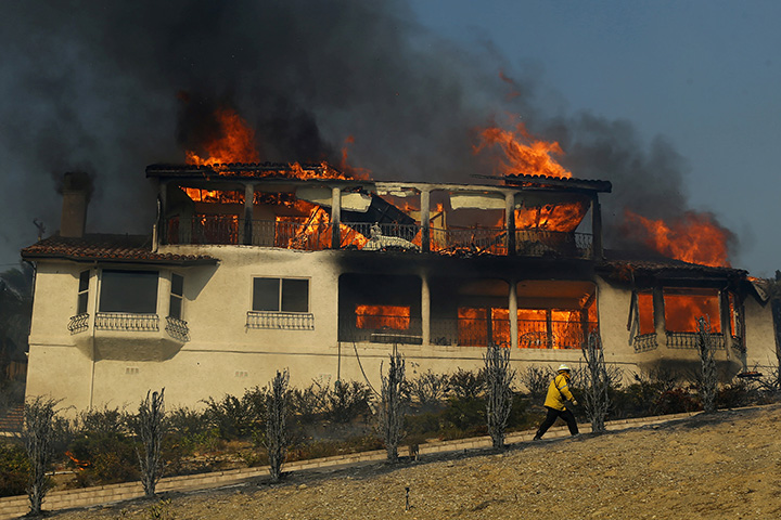 A firefighter inspects a burning home during a wind-driven wildfire in Ventura, California, December 5, 2017.