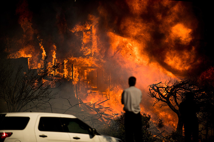 A man watches flames consume a residence as a wildfire rages in Ventura, Calif., Tuesday, Dec. 5, 2017.