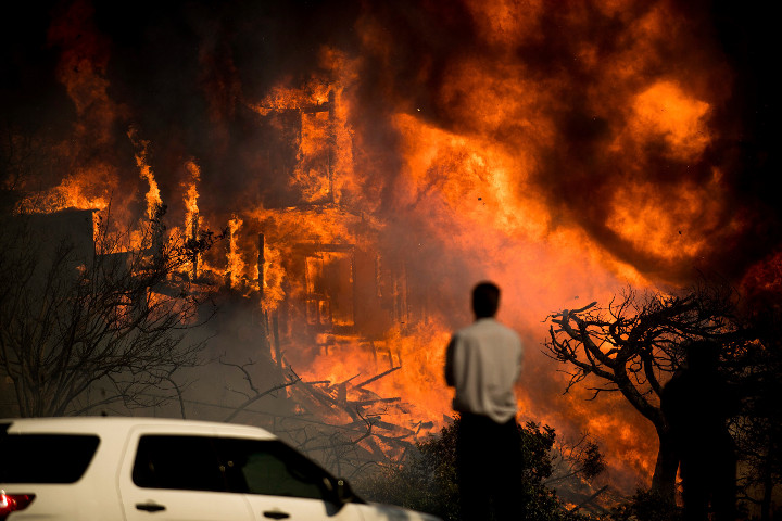 A man watches flames consume a residence as a wildfire rages in Ventura, Calif., Tuesday, Dec. 5, 2017. 
