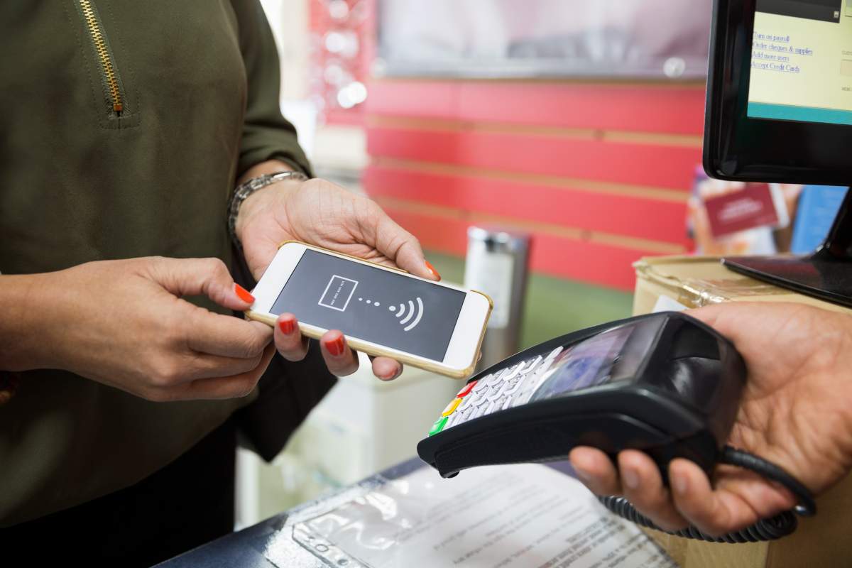 Close up woman paying using smart phone contactless payment in store.