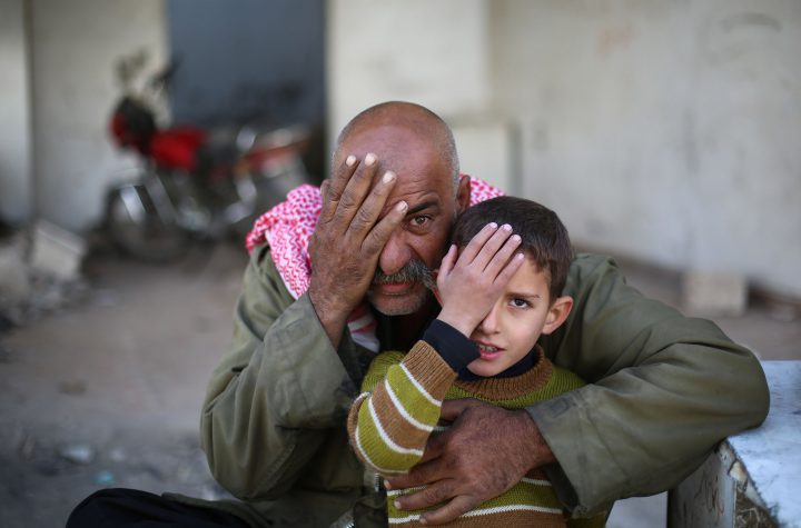 A Syrian man and a child holding hand cover his eye in support of Syrian baby Karim.