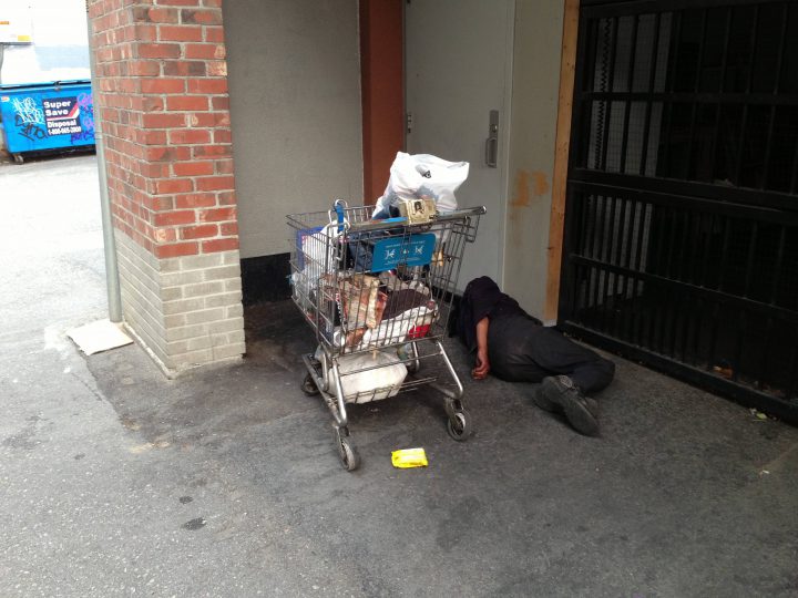 A sleeping homeless man in Kelowna with his shopping cart of belongings. 