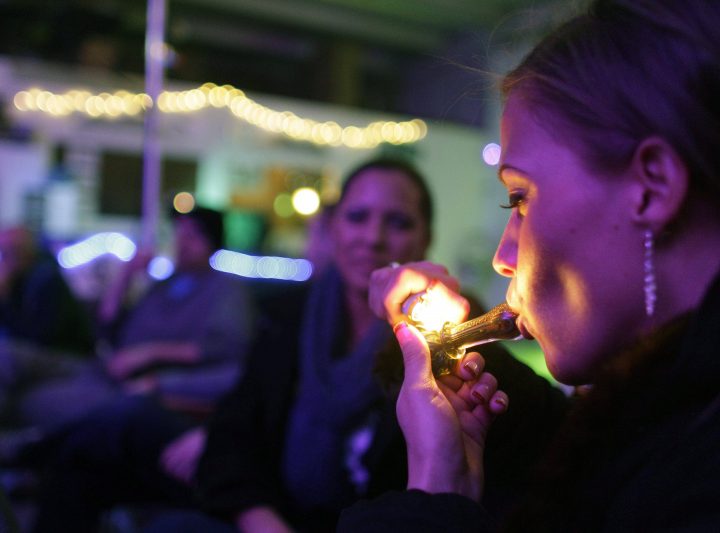 FILE - In this Dec. 31, 2012 file photo, a woman in Denver smokes marijuana on the official opening night of Club 64, a marijuana-specific social club, where a New Year's Eve party was held, in Denver.