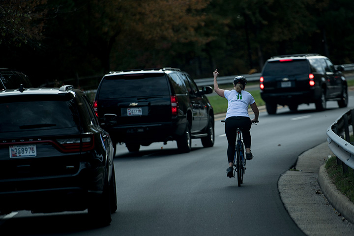 A woman on a bike gestures with her middle finger as a motorcade with U.S. President Donald Trump departs Trump National Golf Course, October 28, 2017 in Sterling, Virginia. 