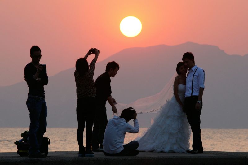 The sun sets behind a couple in wedding dress as they pose for photographers on a wall at a beach in the Stanley district of Hong Kong on October 29, 2010.