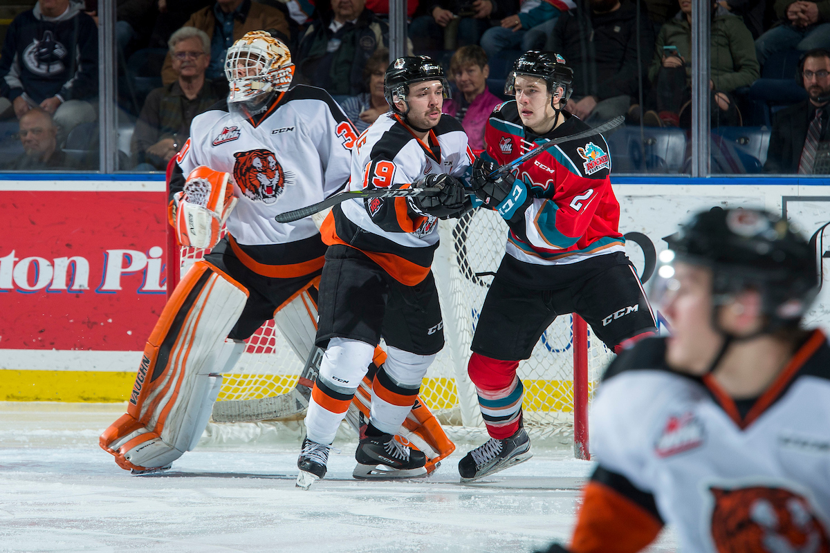 KELOWNA, CANADA - NOVEMBER 25: Kyle Topping #24 of the Kelowna Rockets is checked by David Quenneville #19 in front of the net of Michael Bullion #30 of the Medicine Hat Tigers during second period on November 25, 2017 at Prospera Place in Kelowna, British Columbia, Canada.  (Photo by Marissa Baecker/Shoot the Breeze) .