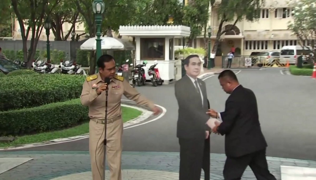 Thailand's Prime Minister Prayuth Chan-ocha, left, directs the scene as a life-sized cardboard cut-out figure of himself is carried into view by an aid, in Bangkok, Thailand.