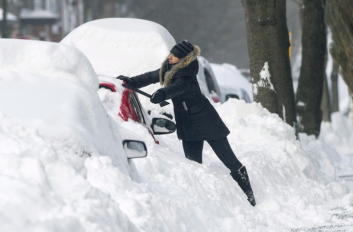 A woman cleans snow from around her car following a major snowstorm in Montreal, Sunday, January 14, 2018. 