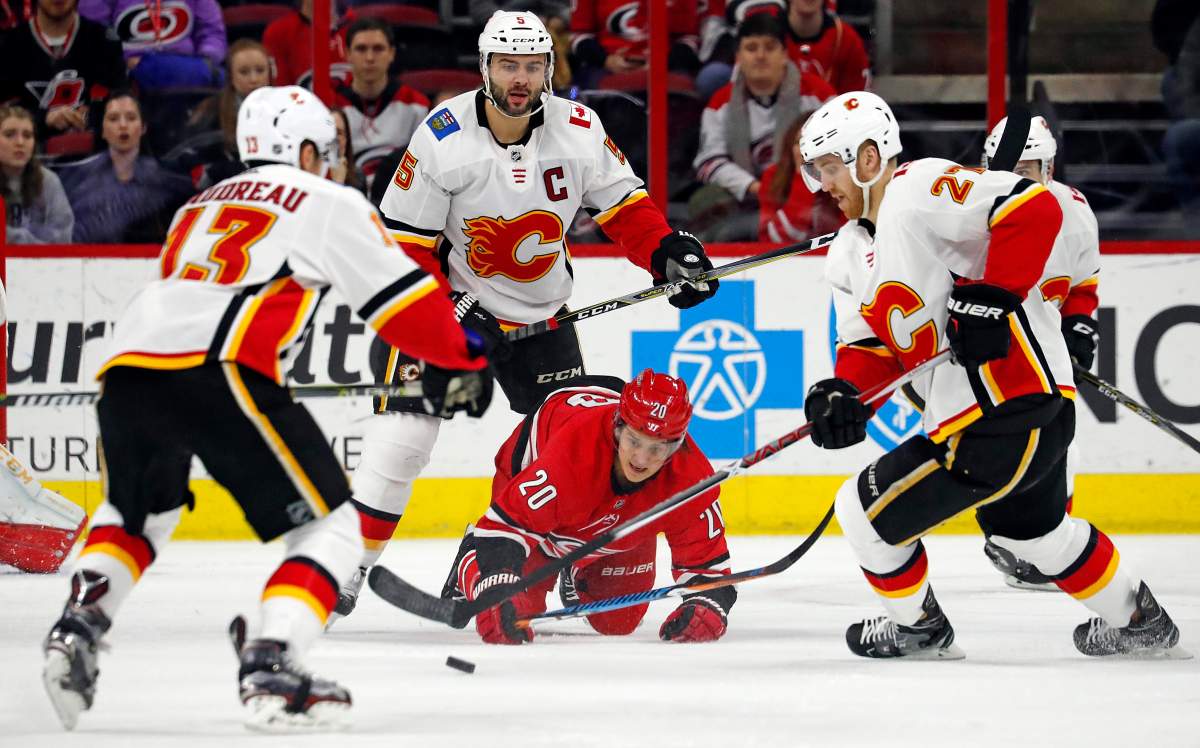 Carolina Hurricanes' Sebastian Aho (20) gets pushed to the ice between Calgary Flames' Johnny Gaudreau (13), Mark Giordano (5), Dougie Hamilton (27) during the first period of an NHL hockey game, Sunday, Jan. 14, 2018, in Raleigh, N.C. 