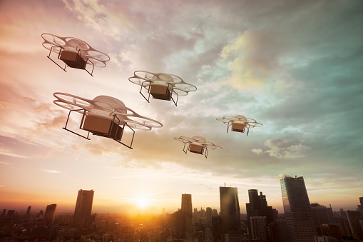 Five delivery drones flying above the city at sunset.